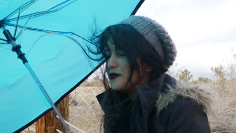 Close-up-on-a-beautiful-young-woman-holding-a-blue-umbrella-in-a-windy-rain-storm-as-bad-weather-comes-in-SLOW-MOTION