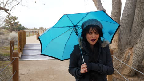 A-cute-woman-smiling-and-walking-in-a-rain-storm-with-a-blue-umbrella-to-protect-her-from-the-strong-winds-and-bad-weather-SLOW-MOTION