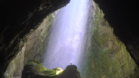 Sunbeam-shinning-on-a-tiny-person-standing-on-a-stalagmite-inside-a-gigantic-cave