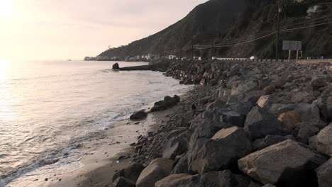 Calm-rocky-shoreline-of-Big-Rock-beach-Malibu-California,-next-to-a-highway-edge-road-at-golden-hour