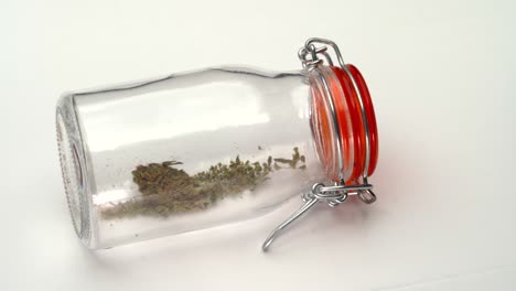 A-slow-pan-reveal-of-a-clear-jar-containing-crushed-marijuana-lying-on-its-side-on-a-white-table