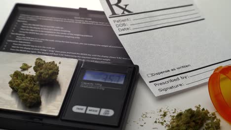 A-digital-scale-measures-grams-of-marijuana,-next-to-a-prescription-note-and-open-pill-bottle-spilling-a-small-pile-of-marijuana