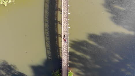 Aerial-view-directly-above-two-people-laying-on-a-footbridge-over-Emerald-Lake-in-Melbourne,-Australia