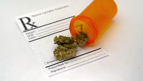 Slow-pan-reveal-of-a-cannabis-prescription-note-and-orange-open-pill-bottle-spilling-marijuana