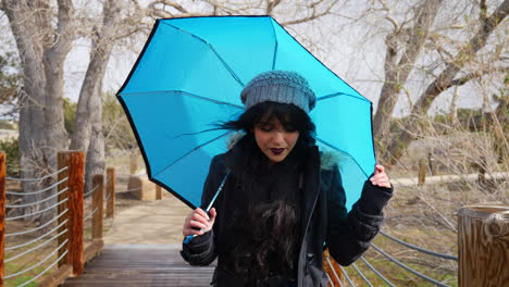 A-pretty-woman-looking-cute-and-smiling-with-a-blue-umbrella-during-a-break-in-the-rain-storm-in-slow-motion