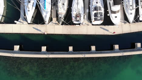 Aerial-view-directly-above-luxury-sailing-yachts-moored-in-a-marina-on-turquoise-water