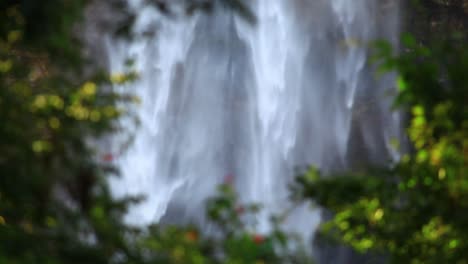 Close-up-footage-of-at-a-waterfall-surrounded-by-green-lush-branches-and-trees