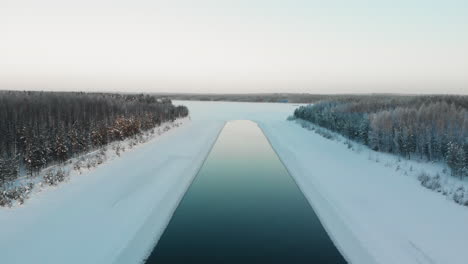 Aerial,-reverse,-drone-shot,-rising-away-from-a-iceless-spot,-on-a-river,-on-a-sunny,-winter-day,-in-Utra,-Joensuu,-North-Karelia,-Finland