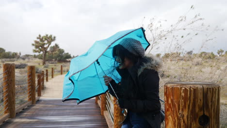 A-pretty-young-woman-smiling-in-bad-weather-with-a-blue-umbrella-during-a-rain-storm-with-strong-wind