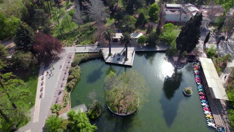 Aerial-view-dolly-in-the-lagoon-of-Quinta-Normal-park-with-pedal-boats,-sunny-day,-trees-and-vegetation-in-the-middle-of-the-city