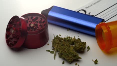 Very-slow-pan-across-a-prescription-note,-blue-vaporizer,-red-grinder,-open-pill-bottle-and-small-pile-of-marijuana-on-a-table