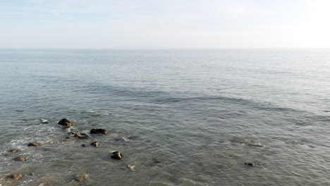 Calm-ocean-waves-of-Big-Rock-Malibu-beach-with-rocks-submerged-in-shallow-waters