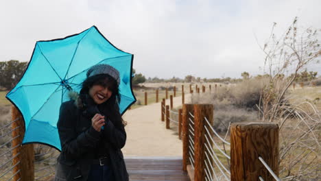 Eine-Hübsche-Frau-Mit-Blauem-Regenschirm,-Die-Bei-Starkem-Wind-Bei-Regensturm-Und-Schlechtem-Wetter-Steht