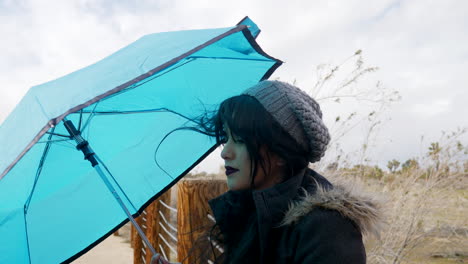 An-attractive-woman-with-a-blue-umbrella-in-bad-weather-as-wind-blows-in-a-rain-storm-under-cloudy-skies