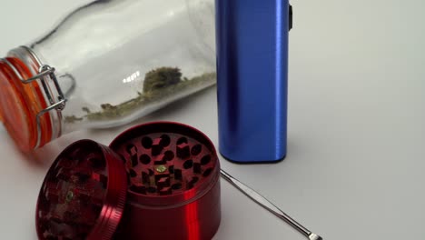 Tight-shot-panning-across-a-metal-scoop,-grinder,-vaporizer,-and-sealed-transparent-jar-of-marijuana-grounds