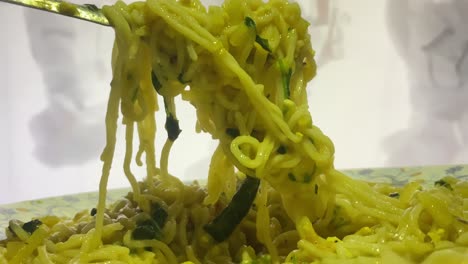 Close-up-shot-of-instant-noodle-with-green-vegetable-been-lifted-with-the-help-of-a-metal-fork-before-eating
