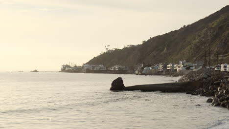 Calm-rocky-shoreline-with-waves-hitting-the-edge,-next-to-the-road-of-Big-Rock-beach-Malibu
