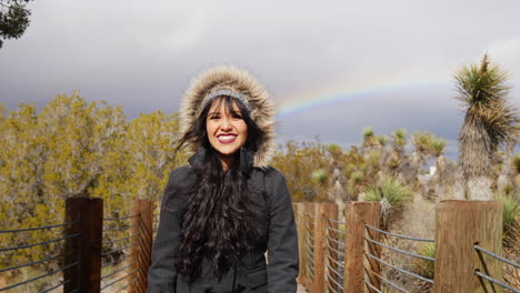Beautiful,-happy-young-woman-in-a-rain-storm-smiling-with-a-colorful-rainbow-in-the-cloudy-sky-after-bad-weather-SLOW-MOTION