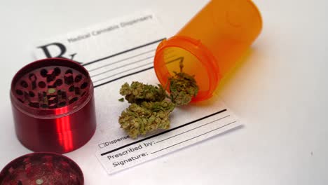 Slow-reveal-of-an-orange-pill-bottle-spilling-marijuana-buds-onto-a-prescription-note-with-a-red-grinder-nearby