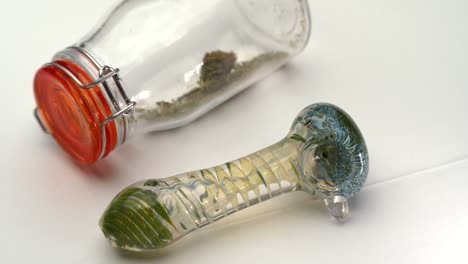 A-colorful-glass-pipe-sits-next-to-a-clear-sealed-bottle-containing-marijuana-grounds