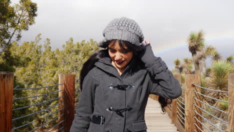 A-pretty-woman-smiling-and-looking-happy-after-a-rain-storm-with-a-rainbow-in-the-cloudy-sky-after-bad-weather-SLOW-MOTION