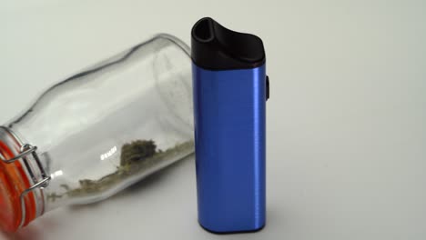 Slow-reveal-of-a-blue-vaporizer-next-to-a-clear-sealed-jar-of-marijuana