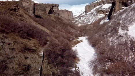 Stairs-leading-to-a-hiking-path-in-a-rugged-canyon-below-cliffs-and-snowy-mountains