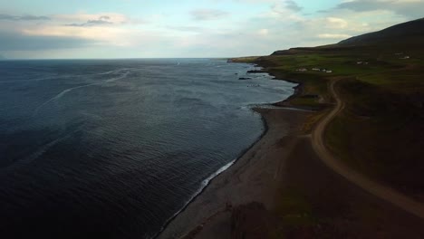 Aerial-panoramic-landscape-view-of-Iceland-north-coast,-with-ocean-waves-crashing-on-the-shoreline,-at-dusk