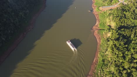 Drone-birds-eye-shot-of-tourist-boat-turning-on-Iguazu-River-during-sunny-day-in-jungle-of-South-America