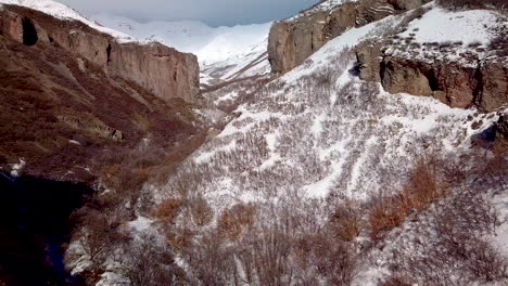 Aerial-view-of-rugged-terrain-with-cliffs-and-snow-covered-mountains-ahead