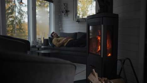 Man-taking-power-nap-in-his-cabin-with-burning-fireplace-to-get-warm,-static-view