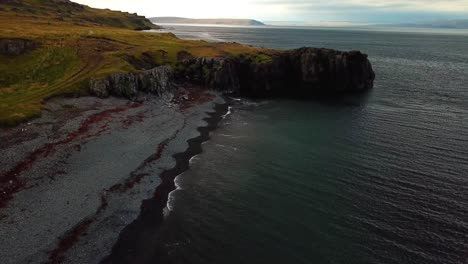 Aerial-landscape-view-of-Iceland-north-coast-cliffs,-with-ocean-waves-crashing-on-the-shoreline,-at-dusk