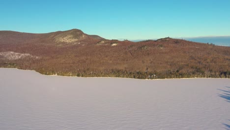 Aerial-SLIDE-over-a-frozen-lake-with-the-hilly-forested-shore-in-the-distance