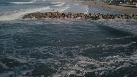 Aerial-drone-view-of-surfer-heading-out-over-ocean-waves-off-coastline-of-Venice-beach