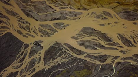 Aerial-top-view-of-a-glacier-river-flowing-in-a-valley,-with-many-branches,-on-dark-sand,-in-Iceland