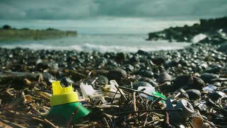 Broken-plastic-waste-lies-washed-up-on-a-beach,-with-waves-breaking-behind