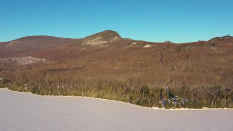 Flying-towards-the-hills-on-the-shore-of-a-frozen-lake-in-Maine-with-a-camp