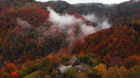 Aerial-tilt-up-reveal-of-a-countryside-house-near-mountain-valley-fall-colored-forest