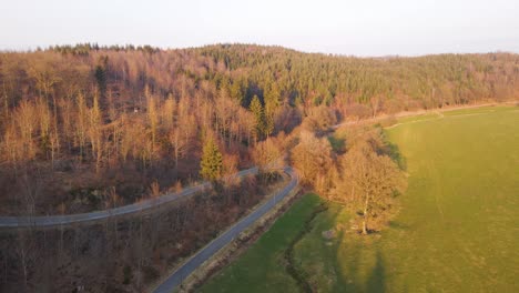 Eine-Steile-Serpentinenstraße,-Die-An-Einem-Sonnigen-Winterabend-Durch-Die-Teilweise-Kahlen-Wälder-Europas-Führt
