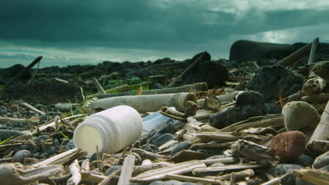 Deep-focus-shot-of-a-washed-up-plastic-battle-lying-on-a-beach-surrounded-by-other-plastic-and-driftwood