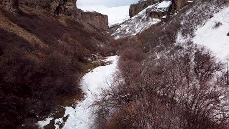 Low-approach-to-a-rugged-and-rocky-winter-landscape-with-cliffs-on-either-side-and-trails-below