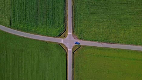 Perfekte-Luftaufnahme-Einer-Symmetrischen-Kreuzung-Mit-Grünen-Feldern-Und-Einem-Vorbeifahrenden-Auto