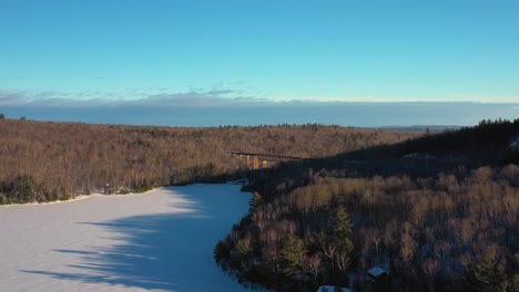 Curving-around-the-shore-line-of-a-frozen-lake-towards-a-railroad-trestle-in-Maine-AERIAL