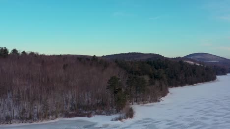 Luftaufnahme,-Die-Entlang-Des-Bewaldeten-Ufers-Eines-Zugefrorenen-Sees-In-Maine-Fliegt