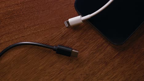 USB-C-and-a-lightning-cable-and-a-phone-on-a-wooden-table-with-moving-light