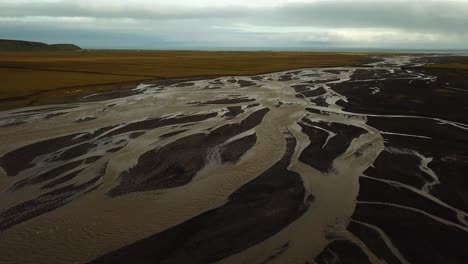 Aerial-landscape-view-of-a-glacier-river-with-many-branches-flowing-in-a-valley,-on-dark-sand,-Iceland