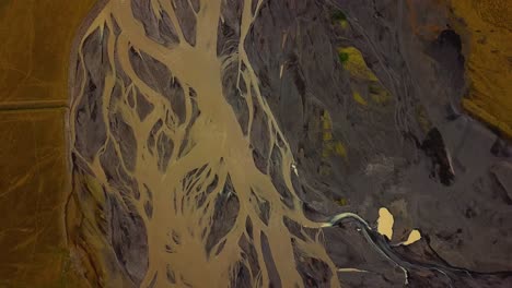 Aerial-top-view-of-a-glacier-river-flowing-in-a-valley,-with-many-branches,-on-dark-sand,-Iceland