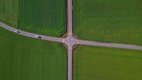 Drone-shot-of-an-X-Crossroad-with-2-cars,-one-going-straight-and-one-taking-a-turn