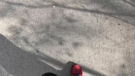 Feet-with-red-shoes-walking-on-grey-asphalt-pavement-on-a-sunny-day-POV