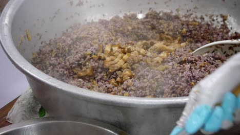 Pork-fried-in-soy-sauce-being-spooned-and-dropped-into-large-pot-of-purple-rice